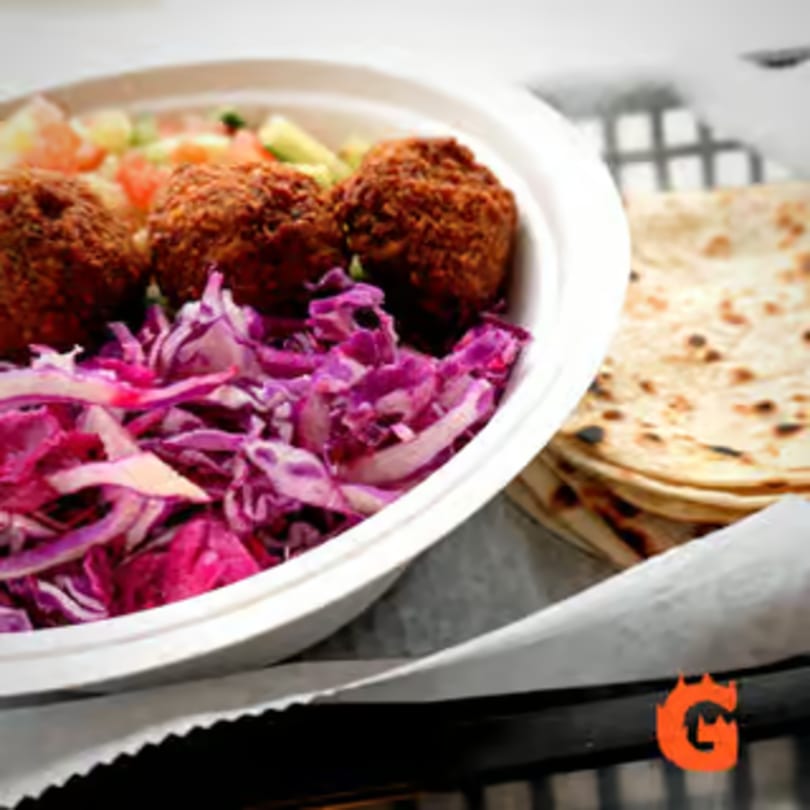 A Mediterranean falafel bowl with red cabbage, diced vegetables, and a stack of pita bread.
