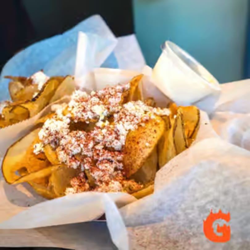 Crispy potato chips topped with feta cheese and red spice, served with a side of white sauce.