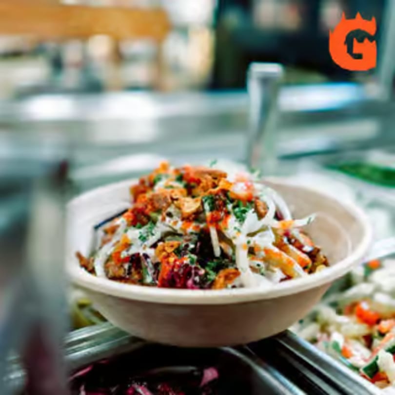 A close-up of a Mediterranean bowl from Gita Pita HTX, topped with meat, sauce, and vegetables.