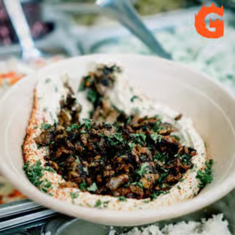 A bowl of Gita Pita HTX hummus topped with seasoned meat, paprika, and fresh parsley.